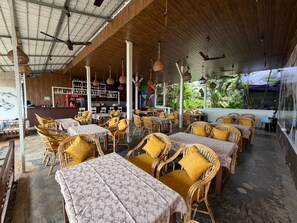 Un caffè all'aperto con mobili in vimini, tavoli, un'area bar e vista sul verde.