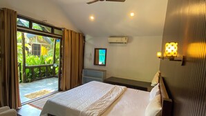 Une chambre d’hôtel équipée d’un lit, d’un bureau, d’un ventilateur de plafond, d’un appareil de climatisation et offrant une vue sur la verdure environnante.