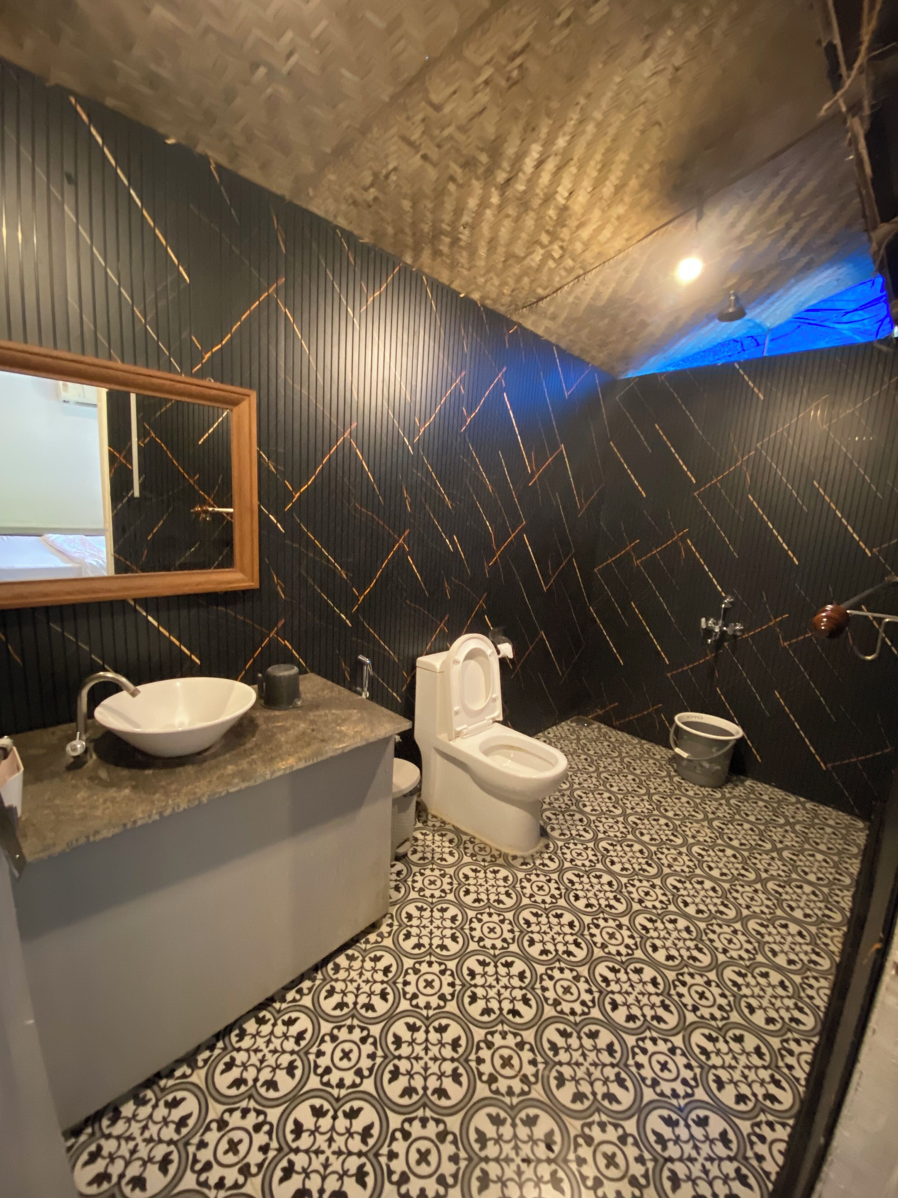 A bathroom with a black and white patterned floor, a white sink, a toilet, and a mirror with a wooden frame.