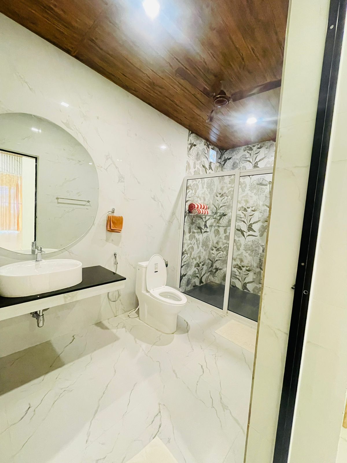 A bathroom with a marble floor, a round sink, a toilet, and a shower with floral wallpaper.
