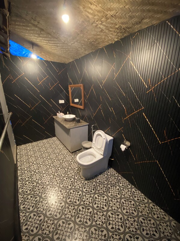 Une salle de bain au design moderne, avec un carrelage décoratif, des toilettes blanches, un lavabo avec un miroir et un plafond à motifs.
