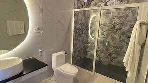 Une salle de bain moderne avec un grand miroir rond, des toilettes et une douche séparée par une paroi de verre.
