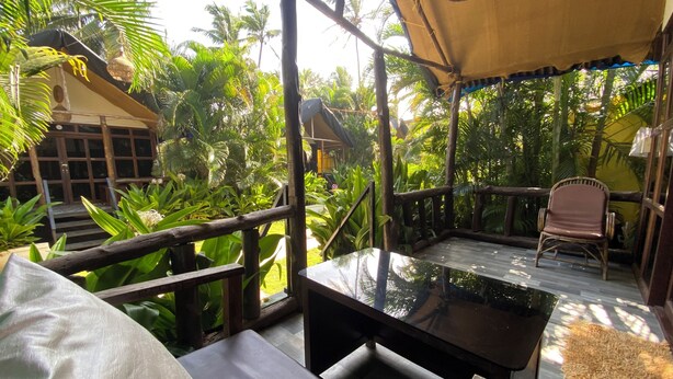 Un espace extérieur aménagé, abrité et doté d’une table et de chaises, entouré d’une végétation tropicale luxuriante et d’une structure en bois en arrière-plan.