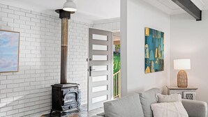 A room with a white brick wall, a wooden floor, a gray sofa, a decorative lamp, and a painting. - Kullaroo Lakehouse - Waterfront Reserve (Summerland Point)