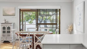 A dining area with a wooden table and chairs, a white cabinet, and a large window with a view of trees and a body of water. - Kullaroo Lakehouse - Waterfront Reserve (Summerland Point)