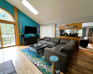 A modern living room with a sectional sofa, a flat-screen TV, a wooden cabinet, and a fish-themed wall decoration.