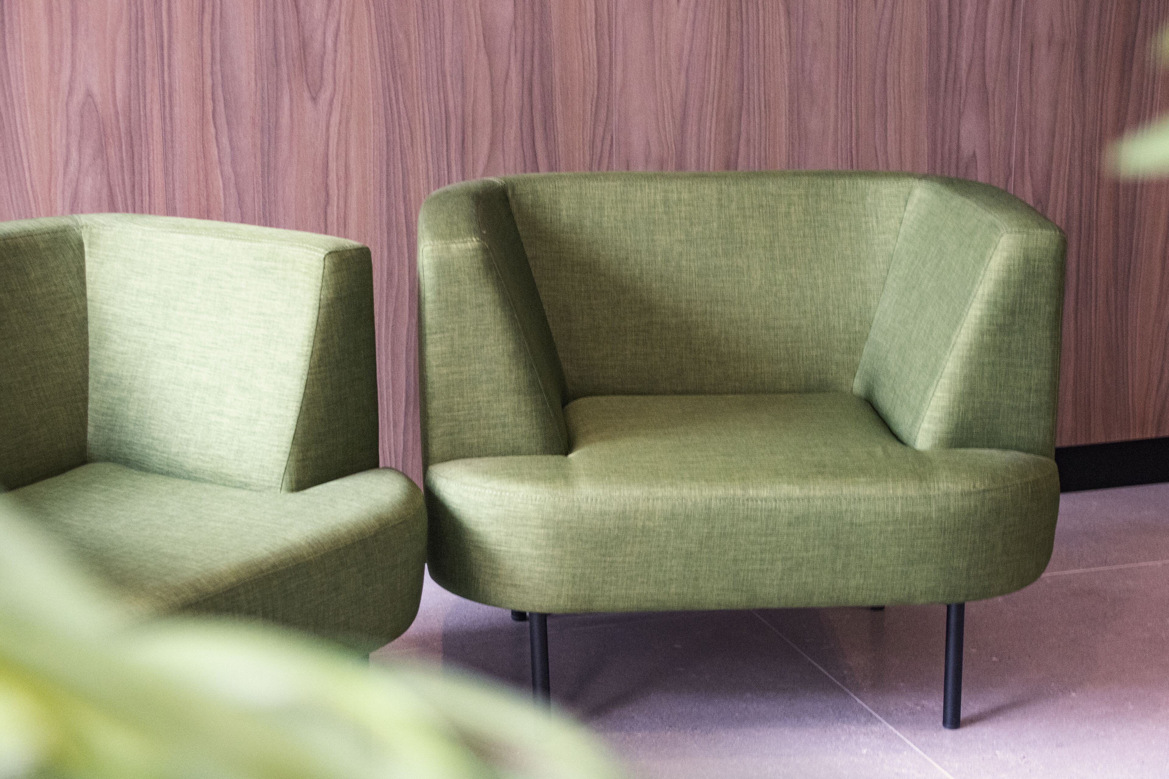 Two green armchairs with black legs, positioned against a wooden wall.