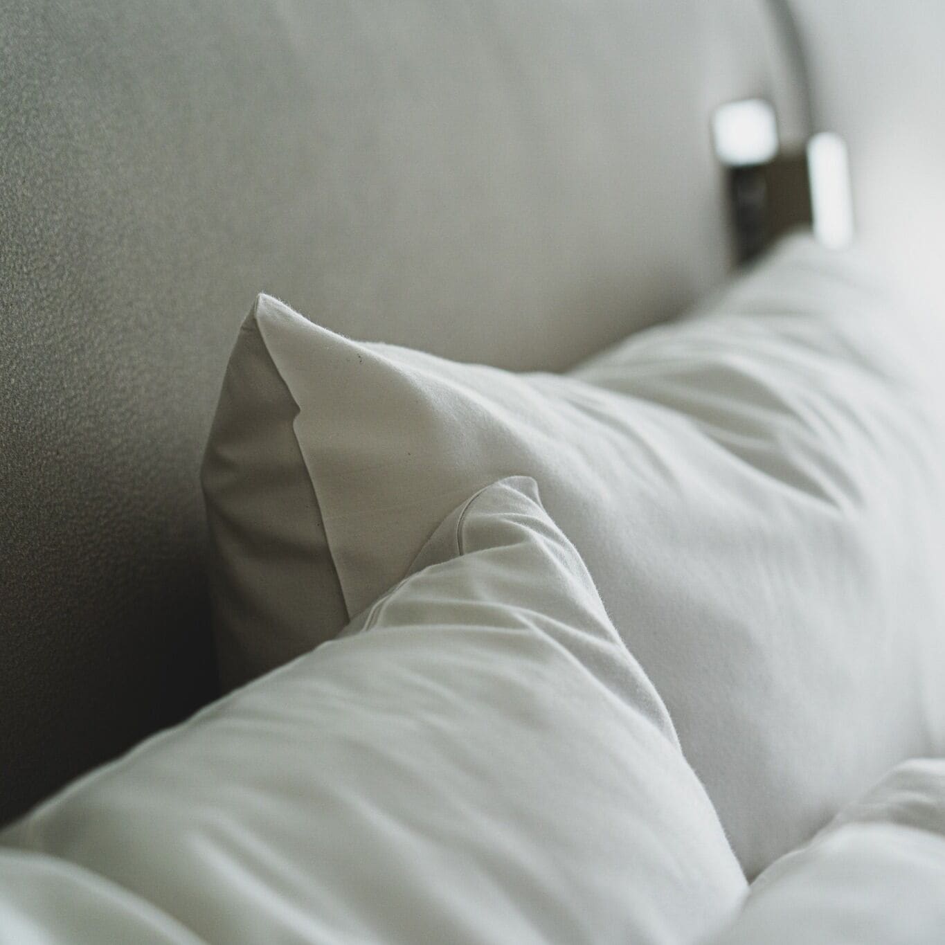A close-up of a bed with white bedding and a grey headboard.