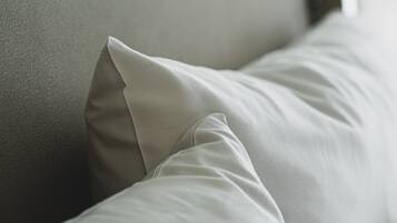 A close-up of a bed with white bedding and a grey headboard.