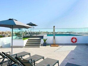 A rooftop terrace with lounge chairs, umbrellas, a pool, and a city view. - Park Heights by the Warren Collection (Msida)