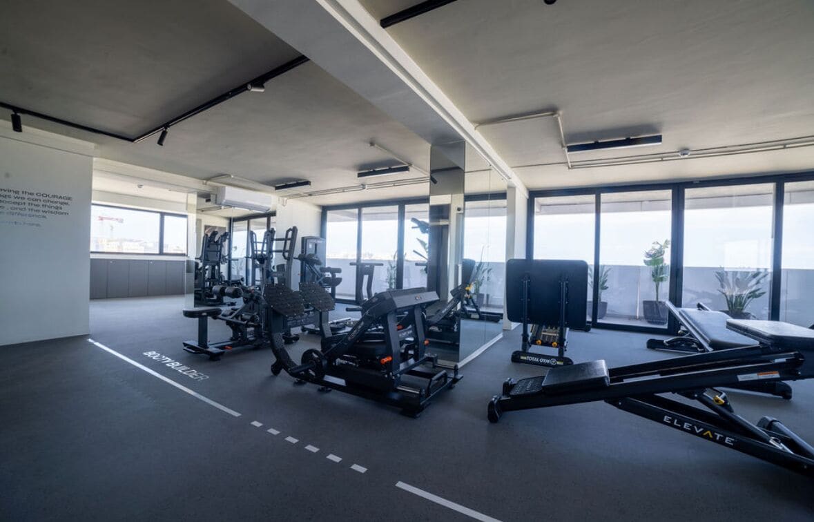 A modern gym with various exercise equipment, large windows, and a view of the city.