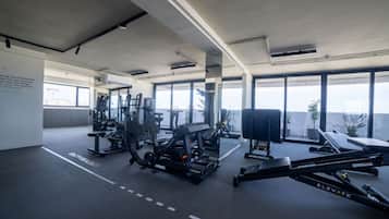 Un gimnasio moderno con diversos equipos de ejercicio, amplias ventanas y vista a la ciudad.