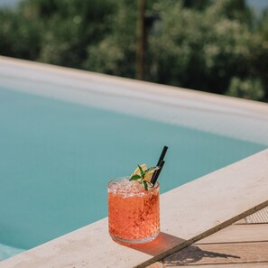 A glass of pink drink with mint garnish and a straw, placed on a wooden deck by a pool. - Park Heights by the Warren Collection (Msida)