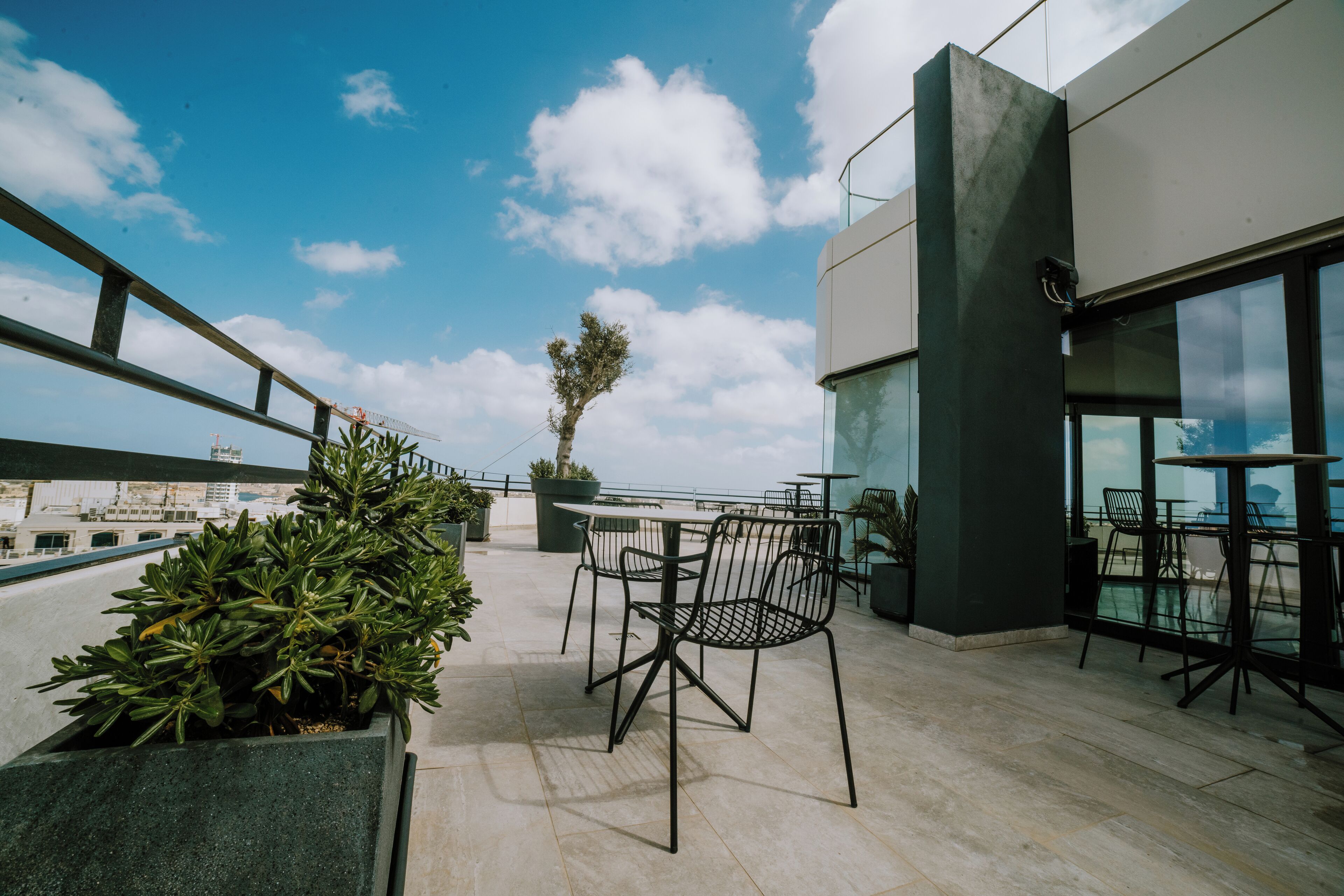 Una terraza en la azotea con mesa y sillas, plantas en macetas y vistas a la ciudad.