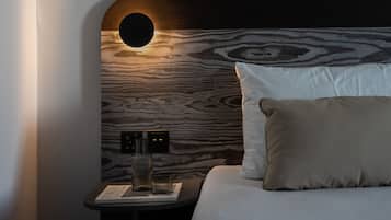 Una habitació d'hotel moderna amb un panell de fusta al capçal, una taula de nit amb una làmpada i un llit ben fet amb almoinos.