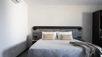 Una cama bien hecha con tablero de madera, dos almohadas, una colcha y una mesita de noche con una lámpara.