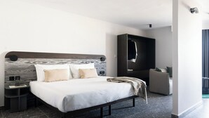 A modern hotel room with a large bed, a dark headboard, a wardrobe, and a seating area. - Park Heights by the Warren Collection (Msida)