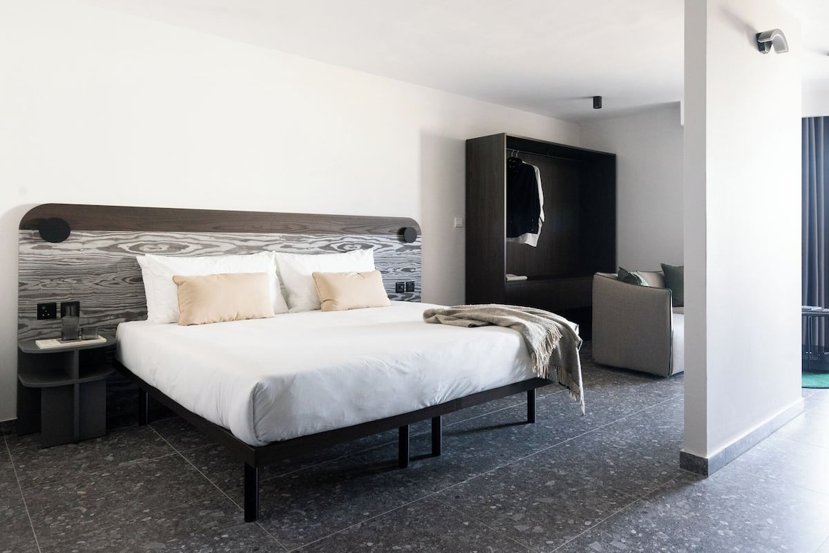 Una camera d'albergo moderna con un letto grande, una testata del letto scura, un armadio e un'area salotto.