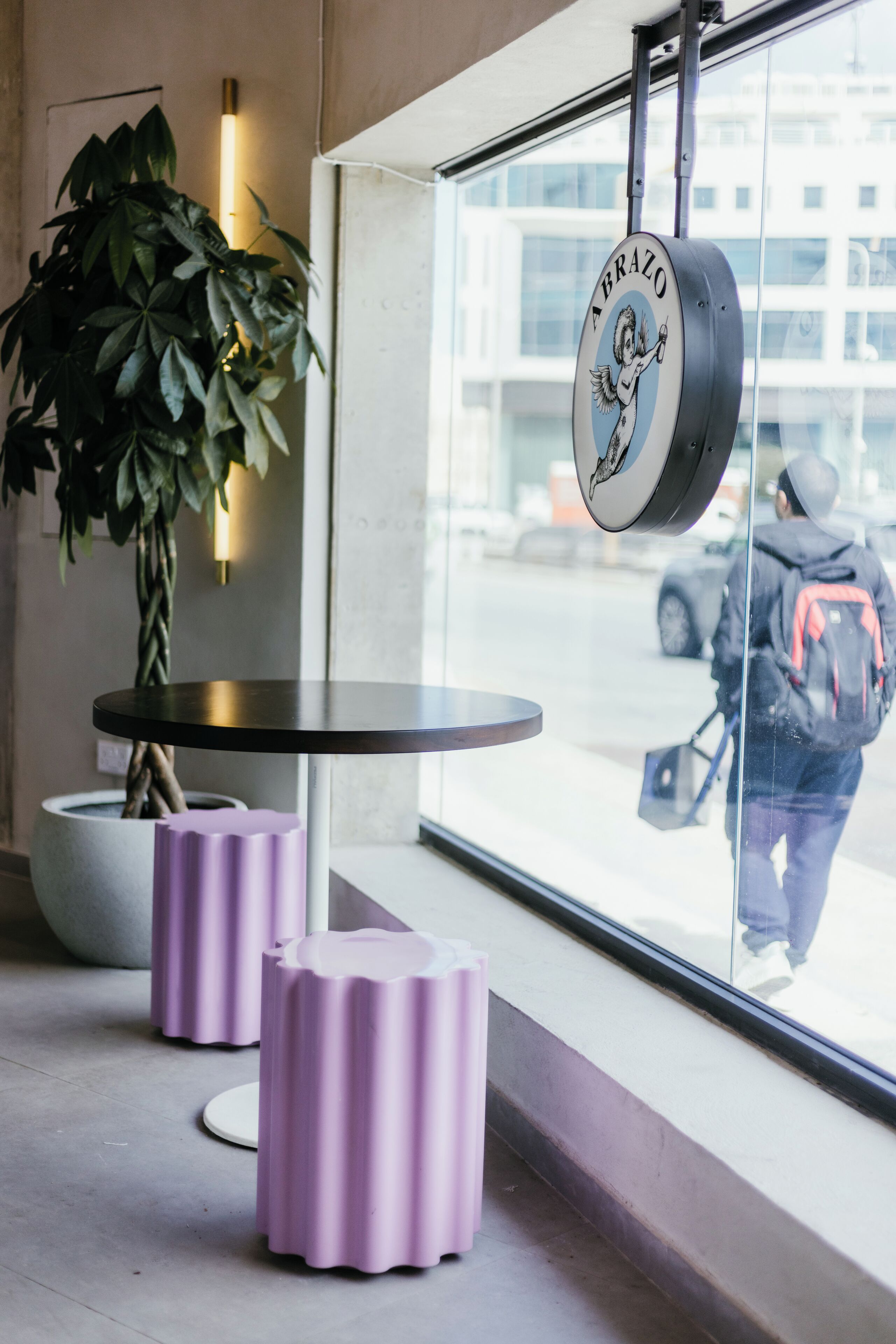 Een modern interieur met een ronde tafel, paarse stoelen, een potplant en een raam met een reflectie van iemand buiten.