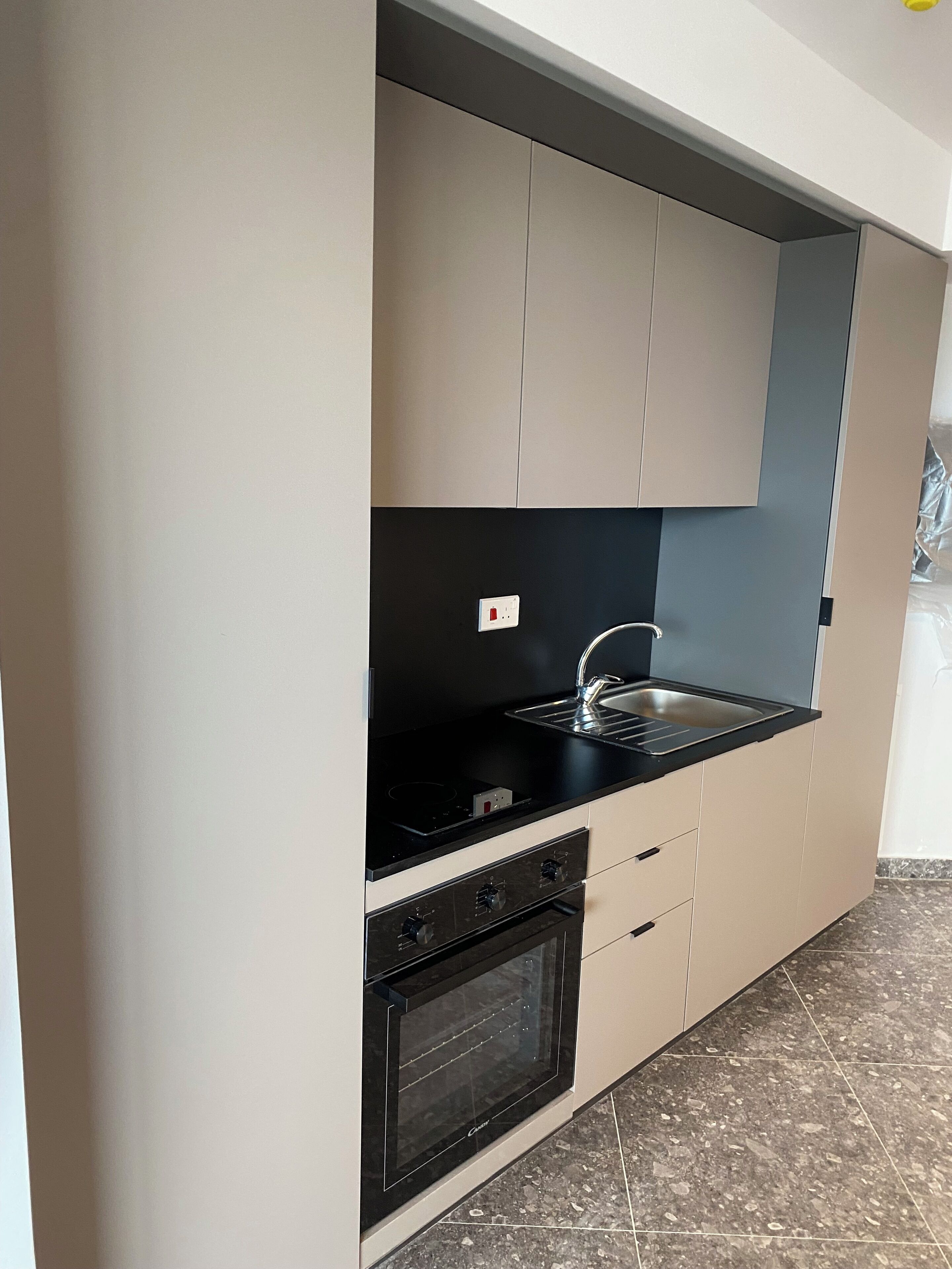 Una cocina moderna con encimera negra, pileta de acero inoxidable y horno empotrado.
