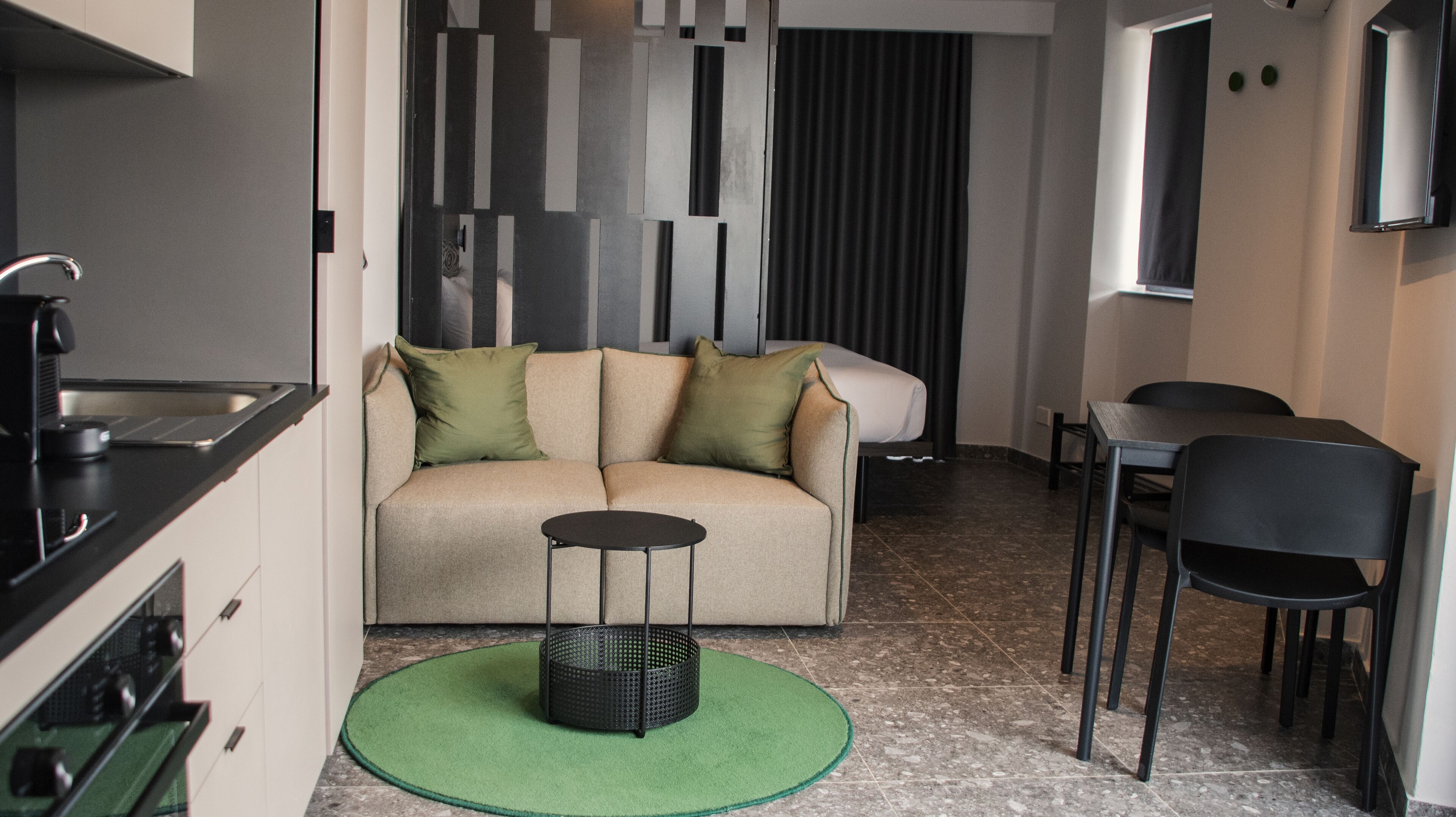 Un espacio habitable compacto con kitchenette, un sofá con cojines, una mesa de comedor con sillas y una mesita redonda con una cesta.