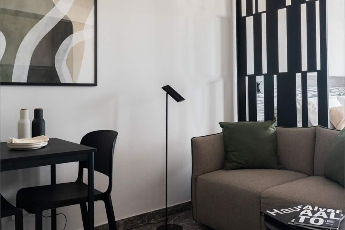 Un soggiorno moderno con un divano, un tavolo da pranzo con sedie, una lampada da terra e un grande quadro astratto.