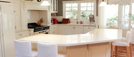 A kitchen with white cabinetry, a central island with bar stools, a stove, and a window with a view of greenery.