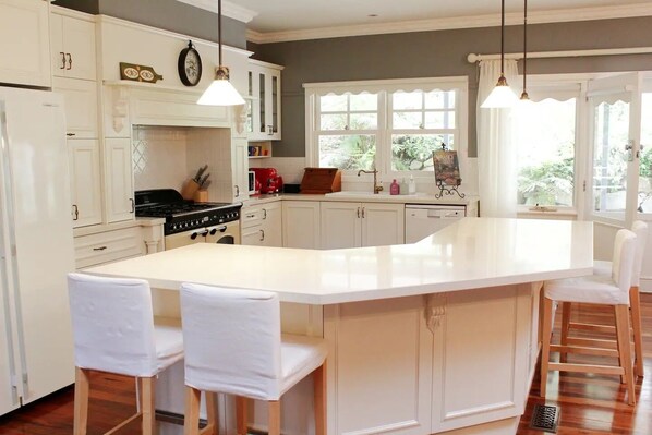 A kitchen with white cabinetry, a central island with bar stools, a stove, and a window with a view of greenery.