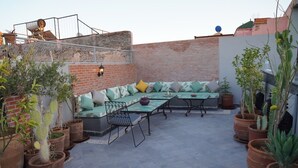 A rooftop patio with a seating area, potted plants, and a table. - Riad Le Petit Joyau (Marrakech)