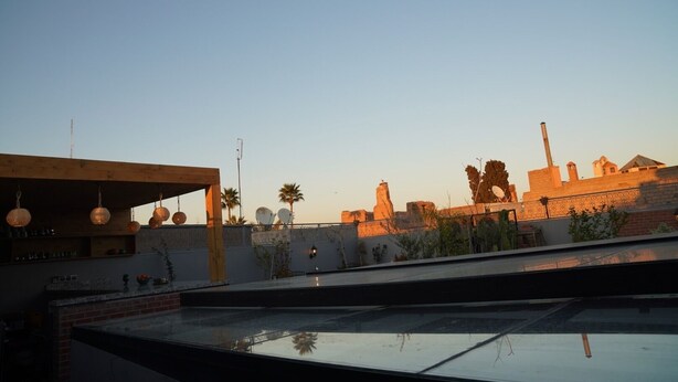A rooftop terrace with a wooden pergola, hanging spherical lights, and a view of historical buildings in the background. - Riad Le Petit Joyau (Marrakech)
