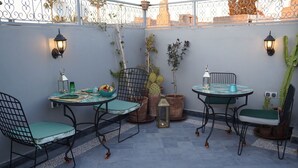 A patio with two tables and chairs, potted plants, and wall-mounted lanterns. - Riad Le Petit Joyau (Marrakech)