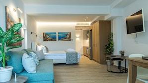 Ein modernes Hotelzimmer mit einer Couch, einem Bett, einem Fernseher und einer kleinen Essecke.