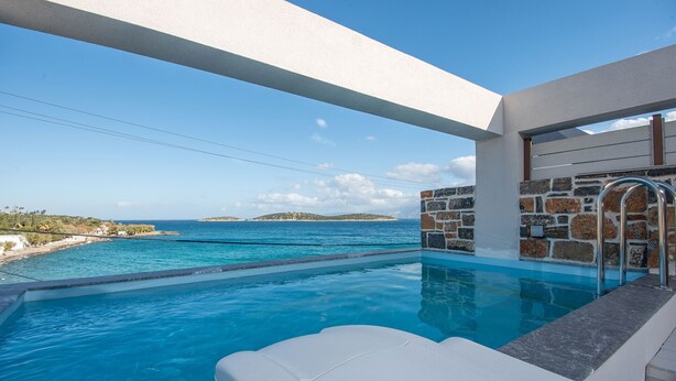Ein Pool mit Blick auf das Meer und Inseln, Steinmauern und einer weißen Lounge-Bereich.