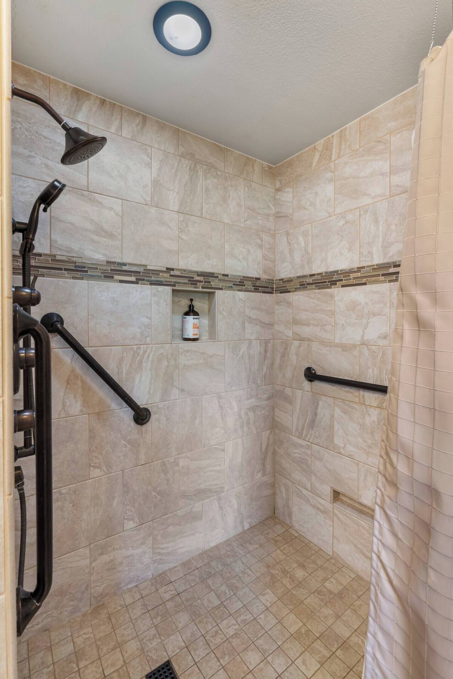 Eine Dusche mit Duschbrause, Haltegriffen und Fliesenboden.