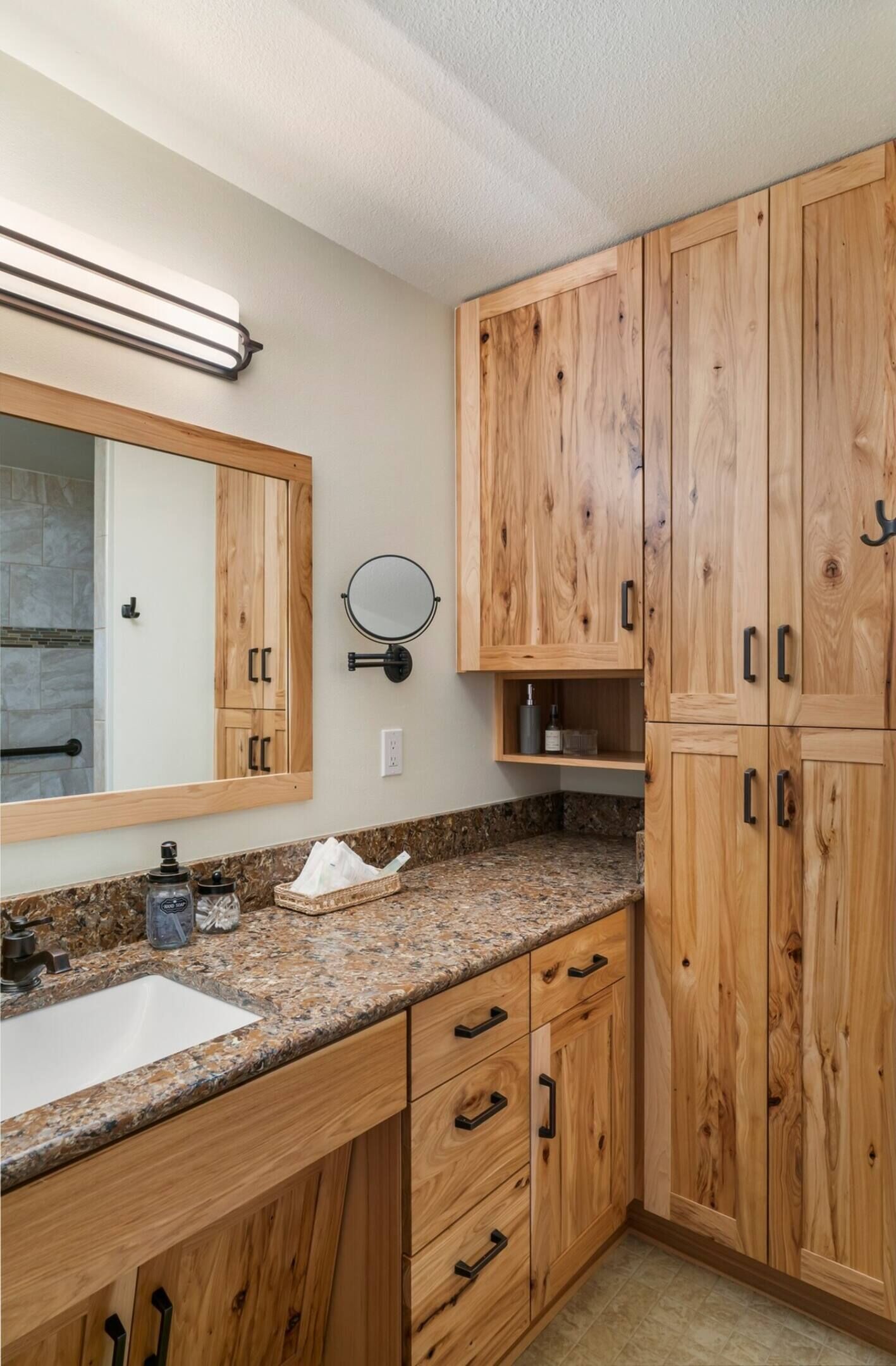 Un baño con armarios de madera, encimera de granito, lavabo y espejo.