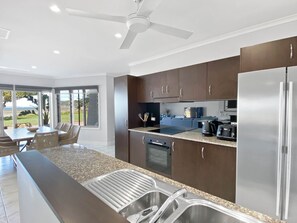 A modern kitchen with a central island, stainless steel appliances, and a dining area with a view. - Magnetic Docks Townhouse 5 (Nelly Bay)