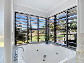 A bathroom with a large bathtub, a window with metal bars, and a potted plant. - Magnetic Docks Townhouse 5 (Nelly Bay)