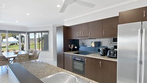 A modern kitchen with a central island, stainless steel appliances, and a dining area with a view. - Magnetic Docks Townhouse 5 (Nelly Bay)
