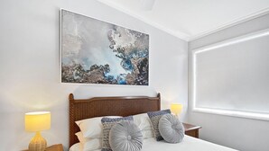 A neatly made bed with a wooden headboard, two bedside lamps, and a large abstract painting above the bed. - Magnetic Docks Townhouse 5 (Nelly Bay)