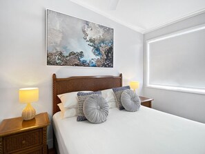 A neatly made bed with a wooden headboard, two bedside lamps, and a large abstract painting above the bed. - Magnetic Docks Townhouse 5 (Nelly Bay)