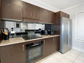 A modern kitchen with dark wooden cabinets, a stainless steel refrigerator, a built-in oven, and a granite countertop. - Magnetic Docks Townhouse 5 (Nelly Bay)
