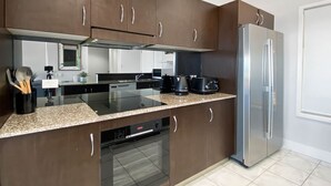 A modern kitchen with dark wooden cabinets, a stainless steel refrigerator, a built-in oven, and a granite countertop. - Magnetic Docks Townhouse 5 (Nelly Bay)