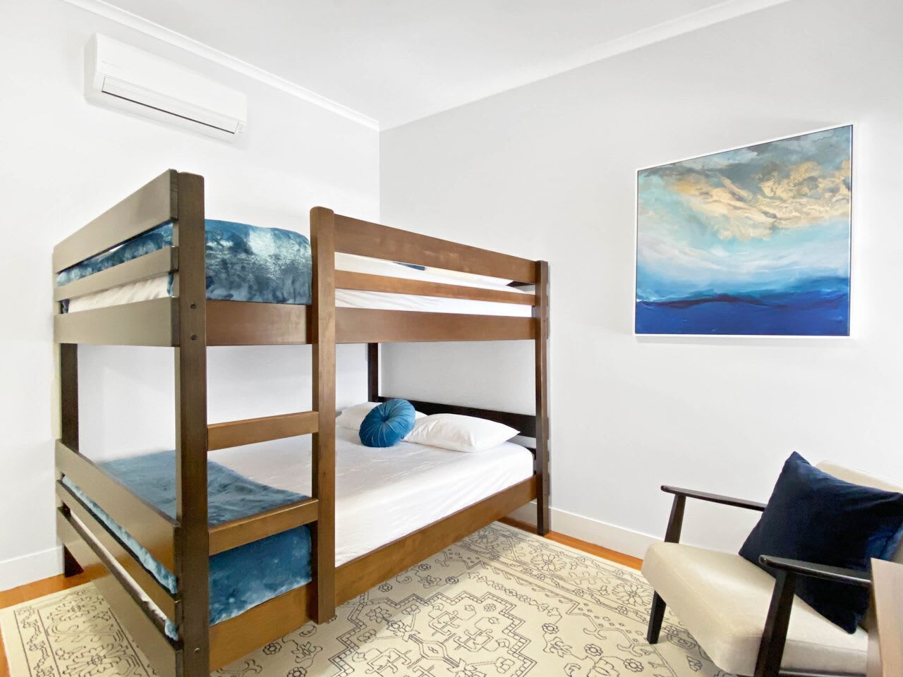 Une chambre avec un lit superposé, un tapis à motifs, une chaise et un tableau accroché au mur.