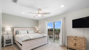 A bedroom with a bed, nightstands, a TV, a wooden cabinet, and a balcony with a view. - Sand Buckets Unit B, Ocean View Beach Townhouse (Mexico Beach)