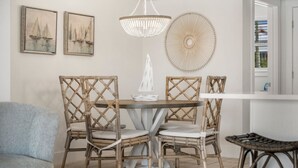 A dining area with a round table, four wicker chairs, a white chandelier, and two framed paintings on the wall. - Sand Buckets Unit B, Ocean View Beach Townhouse (Mexico Beach)
