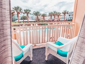 A balcony with wicker chairs and a view of a pool and palm trees. - Waterside Unit 107 Poolside Condo (Mexico Beach)