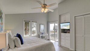 Een slaapkamer met een bed, een bureau, een televisie en een balkon met uitzicht.