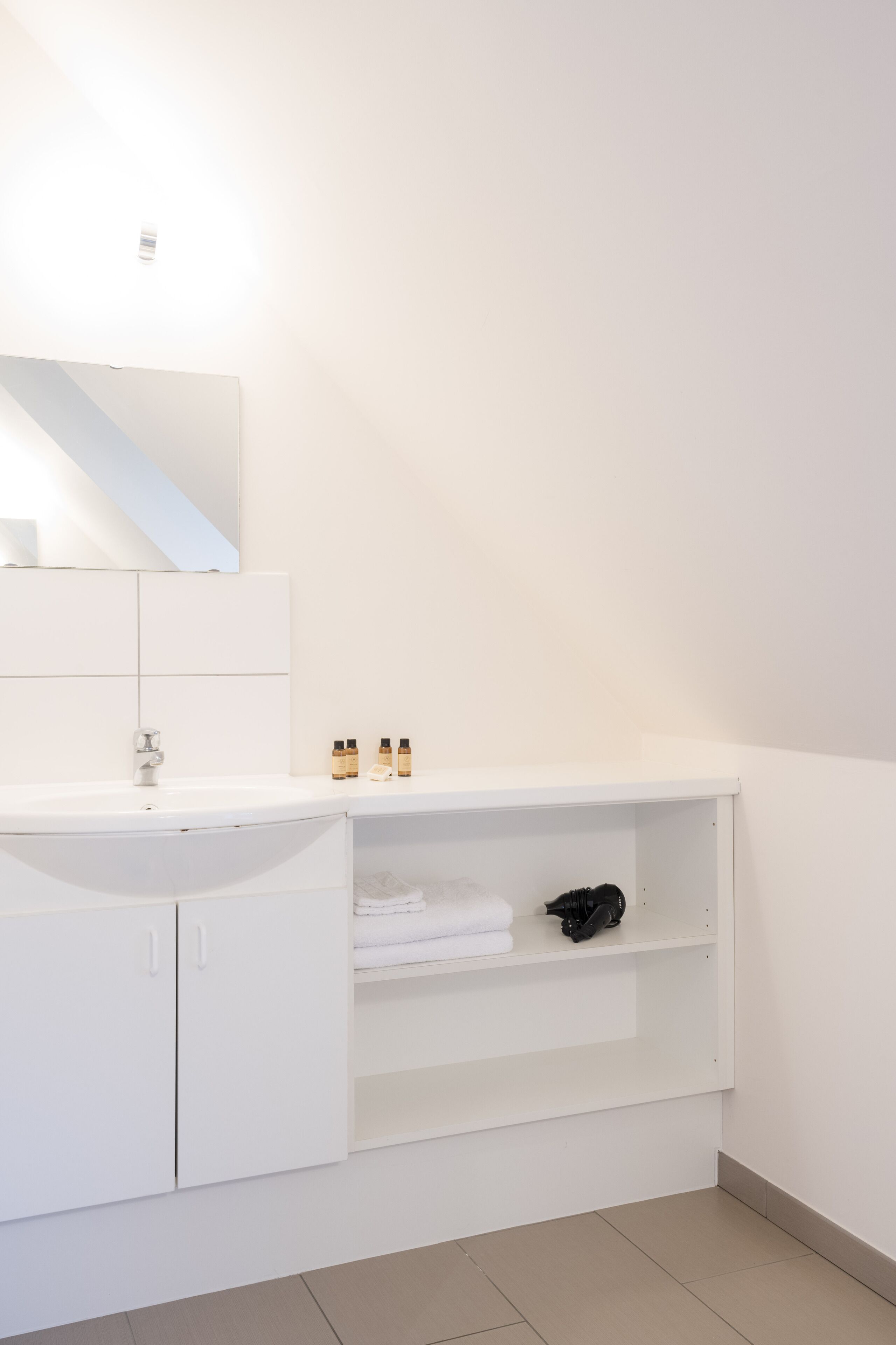 A modern bathroom with a white sink, mirror, and shelves.