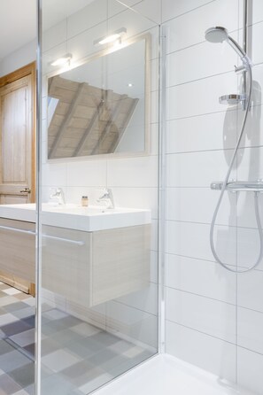 A modern bathroom with a glass shower enclosure, a large mirror, and a white vanity with two sinks.