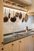 Una cocina con armarios de madera, un lavamanos de acero inoxidable y ollas colgantes.